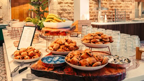 Breakfast buffet with bowls of pastries including croissants and pain au chocolat, fresh fruit and glasses arranged on a marble counter.