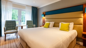 A signature room in The Fairways, with a large double bed and comfortable seating area, by the window, with two chairs and a table.