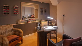Cozy nail salon interior with two chairs, shelves of nail polish, a manicure table, and warm lighting. Relaxing and inviting atmosphere.