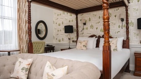 Historic bedroom with a carved four-poster bed, botanical wallpaper and upholstered seating.