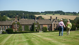 Two guests walking towards the main house at Littlecote House on a sunny day, with a view of fields in the distance