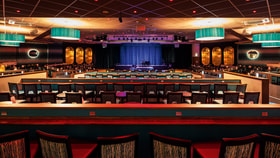 A large auditorium in Sinah Warren's late lounge, featuring rows of chairs and tables arranged for an event.