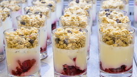 Close-up of layered yogurt parfaits topped with granola and raisins, with fruit compote at the bottom in clear glasses.