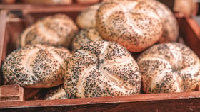 Close-up of round bread rolls topped with poppy seeds, stacked in a wooden crate at a buffet.