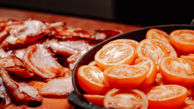Close-up of halved cherry tomatoes in a bowl with slices of cooked bacon blurred in the background.