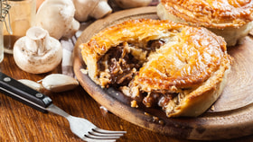Close up of a beef and mushroom pie that has been opened with a fork, releasing delicious flavoursome gravy