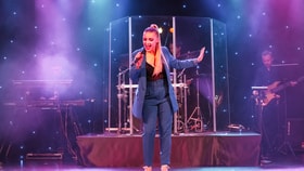 A woman in a blue suit performing on stage at Cricket St Thomas