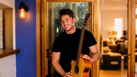 Scott Wilkes smiling whilst holding a guitar and looking off to the side