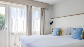 Bedroom featuring a white bed, with large windows letting in plenty of natural light through net curtains