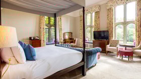 Historic themed bedroom with a four poster bed and large windows framed by floor length curtains