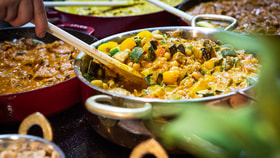 A chef stirring a chickpea curry made for the market kitchen, surrounded by other curries