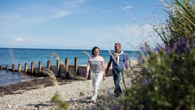 A man and woman stroll together along a serene beach, enjoying the sun and waves.