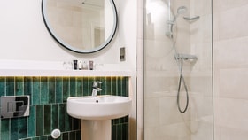 Modern bathroom with a pedestal sink, illuminated round mirror and walk-in glass shower. Green feature tiles and contemporary fixtures create a clean, elegant design.