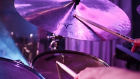 Close-up of a drum kit cymbal and drumsticks under stage lighting.