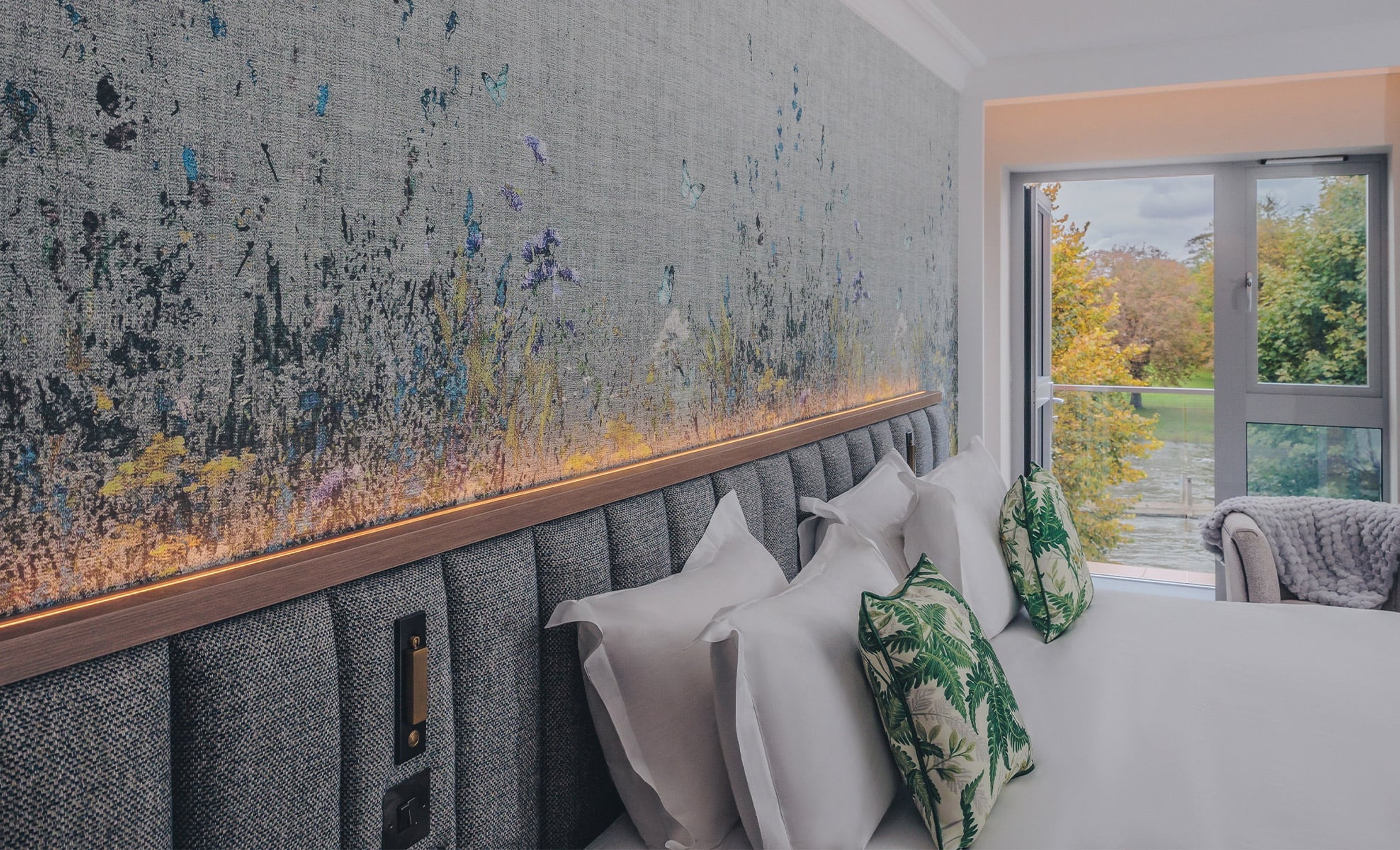 Hotel room with bed with crisp white sheets with a backdrop of a window with a river view