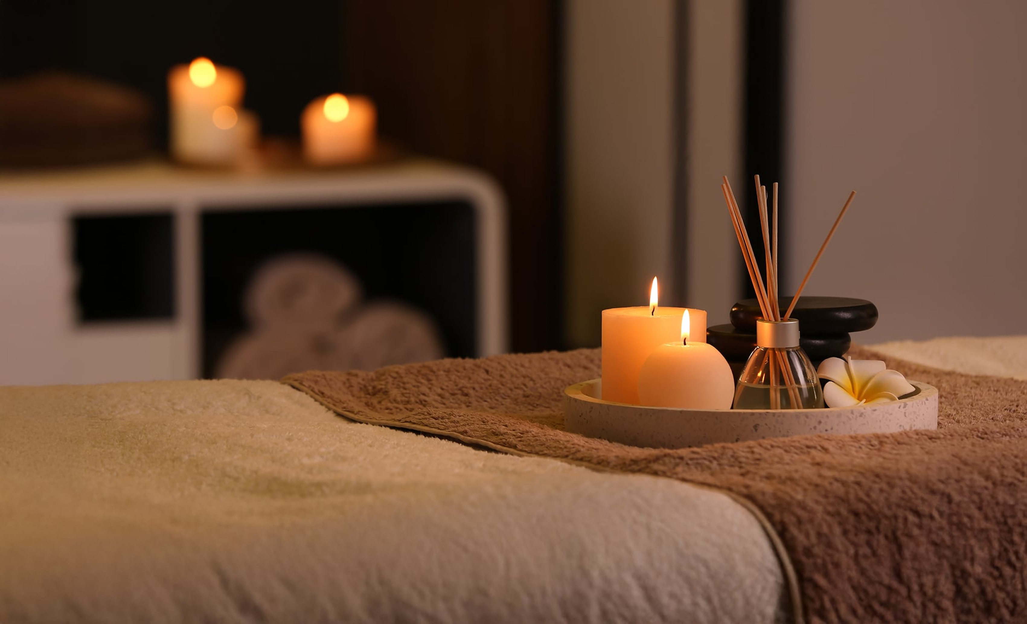 A spa treatment room featuring candles and a soft towel on a treatment bed