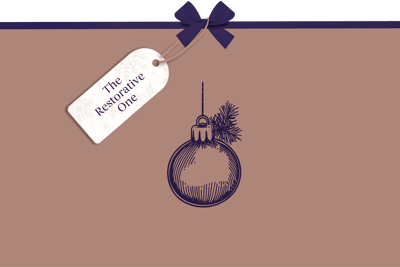 Minimalist festive graphic with a beige background, featuring a dark purple line illustration of a hanging bauble with a small pine sprig. A gift tag tied with a purple ribbon reads ‘The Restorative One’.