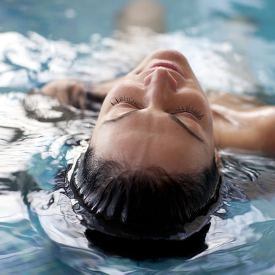 A person lays in the pool with head half submerged, looking very relaxed on a spa day at Warner Hotels