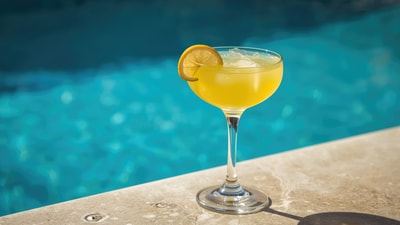 A yellow cocktail placed beside a pool
