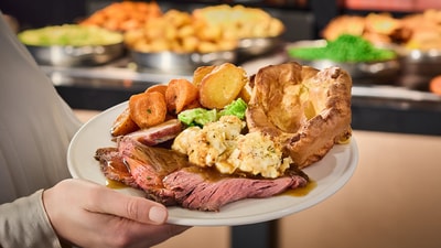 A plate full of roast dinner delights held by someone in front of the carvery selection