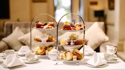 A beautifully arranged tiered afternoon tea featuring cakes, scones, sandwiches, and tea cups on an elegantly set table.
