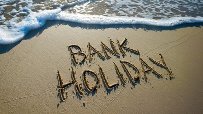 Bank holiday written in the sand with a wave approaching the message