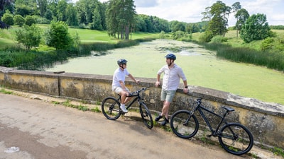 A couple of guests stand with their bikes, taking a rest and taking in the beautiful views of the grounds at Heythrop Park