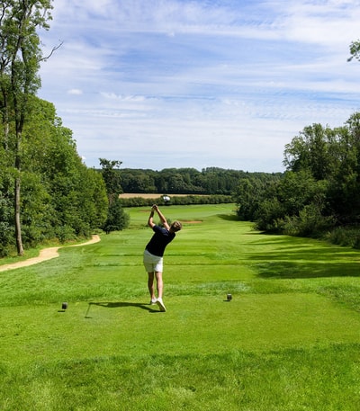 A man playing golf, standing in with the golf club above is head after taking a shot