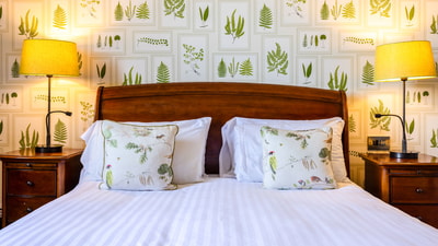 Cosy hotel bedroom with botanical wallpaper, wooden headboard and bedside lamps.