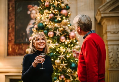 Two people stood in front of a Christmas tree and drinking prosecco