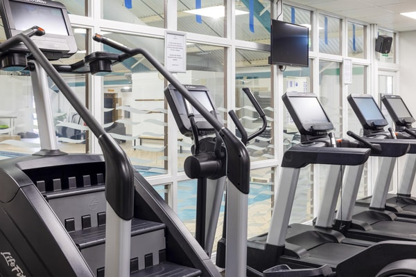 Gym with cardio equipment, including treadmills and stair climbers, overlooking the indoor swimming pool.
