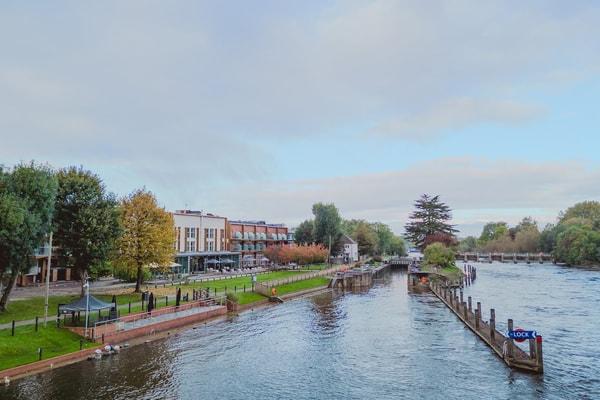 A tranquil stretch of the Thames framed by lush greenery and charming riverside architecture, capturing the serene beauty surrounding the hotel.