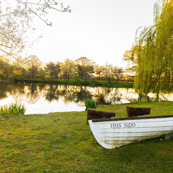 HMS Nidd rests on the ground beside the lake, bathed in the golden glow of sunset - a peaceful, picturesque spot to discover on your adventures.