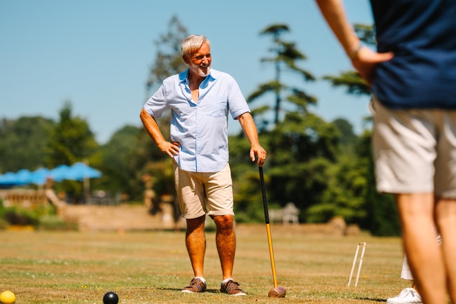 Two people enjoy a relaxed game of croquet on a sunny lawn, mallets in hand and wickets set across the grass.