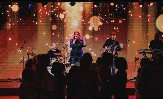 A band performs energetically on stage, captivating the audience in front of a vibrant large screen backdrop.