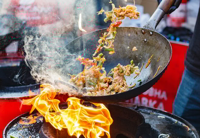 Close up of a pan with the chef tossing ingredients over a flame at a cooking showcase