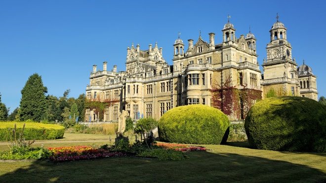 Thoresby Hall - A grand historic mansion with intricate architecture, surrounded by manicured gardens and vibrant flowerbeds under a clear blue sky.
