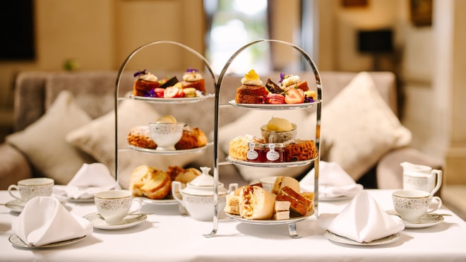 A three-tiered stand displaying an assortment of pastries, cakes, and scones, accompanied by elegant teacups and napkins.