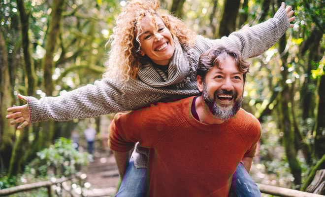 Couple enjoying freedom, a woman on the back of a man carrying her with her arms spread open.