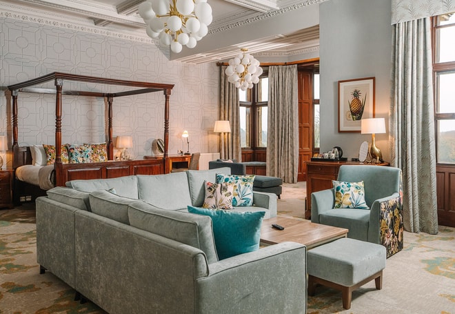 A large bedroom with neutral and pale blue decor, a dark wood four poster bed and plenty of natural light flowing through the window