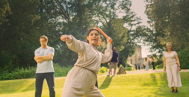 Angie stands firm with an axe ready to throw at the target, Mick looks on in the background with slight concern