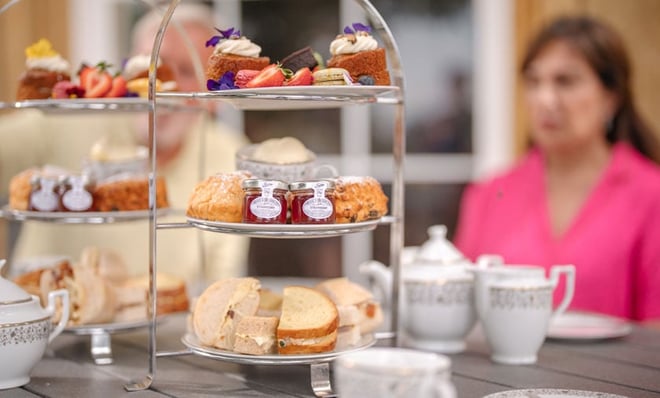 A tiered dessert stand showcases an array of colorful pastries, scones, and jams, accompanied by fine china tea set on a table.