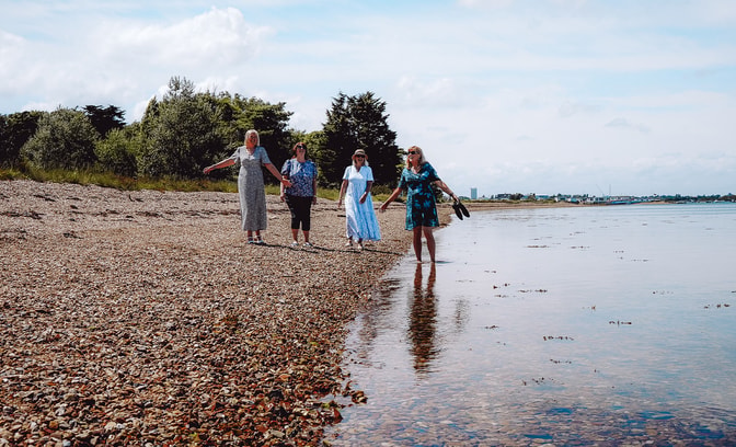 A group of people walking along the sandy beach at Sinah Warren, enjoying the sunny day and ocean views.