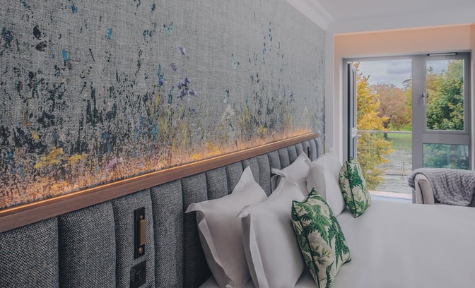 Hotel room with bed with crisp white sheets with a backdrop of a window with a river view