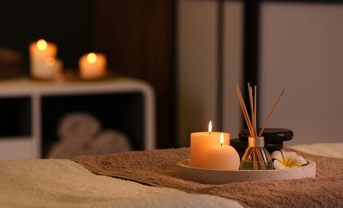 Spa treatment room with lit candles, diffuser reeds and towels creating a calming atmosphere