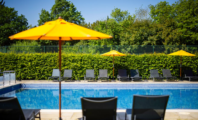 Outdoor pool surrounded by shrubs and featuring deck chairs and yellow parasols