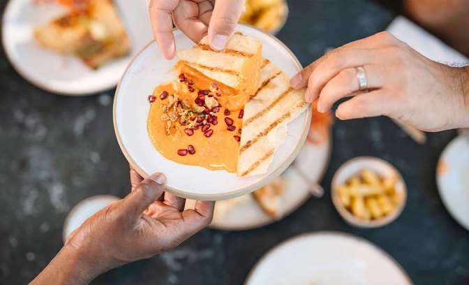 Guests sharing grilled flatbread with dip, garnished with pomegranate seeds, as part of a small plates dining experience.