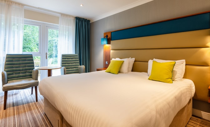A signature room in The Fairways, with a large double bed and comfortable seating area, by the window, with two chairs and a table.