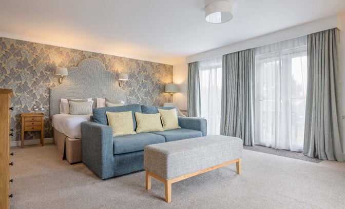 Royal bedroom with a king-size bed, sofa seating area, patterned feature wall, and floor-to-ceiling curtains.