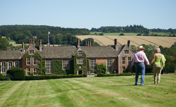 Two guests walking towards the main house at Littlecote House on a sunny day, with a view of fields in the distance